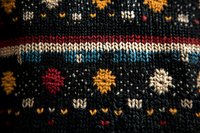 Close-up macro shot of traditional winter knitted pattern with colorful snowflakes and geometric ornaments on dark wool fabric background.