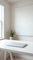 Minimalist white workspace with closed laptop on clean desk near window with small potted plant in bright modern office interior for productivity and focus.