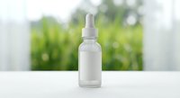 White frosted glass dropper bottle with pump dispenser on clean surface against blurred green foliage background for skincare and cosmetic products.