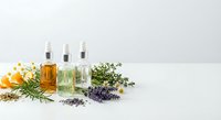 Natural essential oil bottles with fresh herbs and flowers on white background for aromatherapy wellness and organic skincare products.