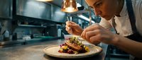 Professional male chef carefully plating gourmet dish with tweezers in modern restaurant kitchen, culinary artistry and fine dining preparation.