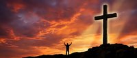 Person with raised arms celebrating near large cross silhouette against dramatic orange sunset sky with clouds on mountain peak for spiritual worship concepts.
