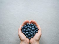 Hands holding fresh blueberries in heart shape on gray background, representing healthy eating, nutrition, and wellness for food and lifestyle content.