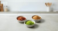 Three ceramic bowls containing colorful spices and seasonings arranged on clean kitchen counter for culinary cooking and food preparation.