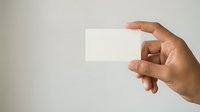 Male hand with medium skin tone holding blank white business card against neutral background, suitable for corporate branding and professional identity mockups.