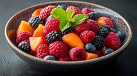 Fresh mixed berries and melon pieces in rustic ceramic bowl garnished with mint leaf, vibrant healthy fruit composition on dark background.