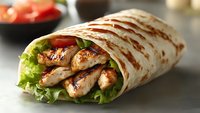 Grilled chicken wrap with fresh lettuce and tomato on white tortilla, served as healthy fast food option for lunch.