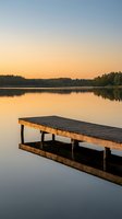 Wooden dock extending into calm lake at sunset with golden sky reflection and forest silhouette creating peaceful waterfront scene for relaxation concepts.