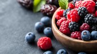 Fresh organic berries in wooden bowl on dark stone background, selective focus on ripe raspberries, blackberries and blueberries for healthy eating concept.