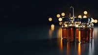 Amber glass vials with metal caps containing liquid samples on dark surface with warm bokeh lights creating laboratory atmosphere for research and testing.