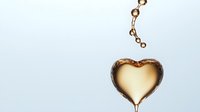 Golden heart-shaped liquid drop with splashing droplets above on white background. Luxury oil, honey or cosmetic serum concept for skincare and beauty.