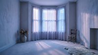 Morning sunlight streams through bay windows into an empty room with sheer curtains, casting soft shadows on pale blue walls and wooden floor, suitable for interior design, real estate, and home staging projects.