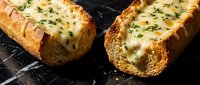 Grilled garlic bread with melted cheese and fresh herbs on dark slate surface. Perfect appetizer for Italian cuisine and comfort food recipes.