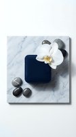 Luxury spa composition with white orchid flower, dark blue velvet jewelry box and smooth black stones on elegant marble surface for wellness branding.