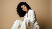 Professional African American businesswoman in elegant white suit smiling confidently against neutral beige background for corporate branding and marketing materials.