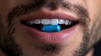 Close up of smiling mouth with blue pill capsule between teeth against dark background, showing medication intake or pharmaceutical concept. Medical and healthcare theme.