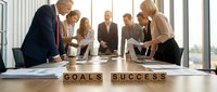 Business team collaborating around conference table with wooden letter blocks spelling goals success in modern office meeting room.