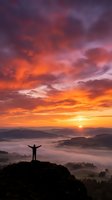 Silhouette of person with raised arms celebrating success on mountain peak at dramatic sunrise with colorful sky and misty valley below for motivation concepts.