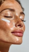 Close-up of woman with freckles applying facial moisturizer, eyes closed, glowing skin and natural makeup. Perfect for skincare advertising.