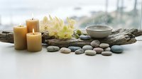 Spa wellness setup with burning candles, smooth stones, white orchids and ceramic bowl creating peaceful relaxation atmosphere for massage therapy.