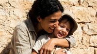 Mother embracing young son against ancient stone wall, showing maternal love and family bonding in warm natural lighting for parenting and relationship concepts.