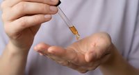 Healthcare professional administering liquid medication with dropper into patient's palm for precise dosage control in medical treatment setting.