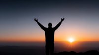 Person silhouette with raised arms celebrating success at sunrise or sunset with dramatic sky and mountain landscape horizon for motivation concepts.