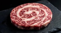 Raw marbled beef steak with intricate fat patterns on dark slate surface, premium cut ready for grilling, cooking preparation and culinary presentations.
