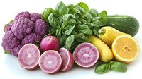 Fresh organic produce arrangement with purple cauliflower, watermelon radish slices, basil leaves, zucchini, and lemons on white background, healthy eating concept.