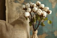 Cotton flowers bouquet in rustic glass vase wrapped with twine rope against vintage turquoise background and burlap fabric, natural home decor styling.