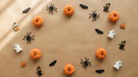 Halloween decorations with orange pumpkins, black spiders, bats and white ghosts arranged on beige background for autumn seasonal crafts and party planning.