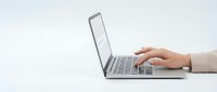 Professional woman hands typing on modern silver laptop computer on clean white desk surface for business and technology applications.