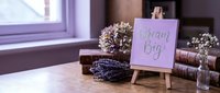 Wooden easel with Dream Big sign beside dried lavender bouquet and vintage books on rustic table, soft natural light, cozy home decor.