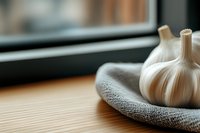 Fresh garlic bulbs in rustic stone bowl on wooden kitchen counter with natural window light creating warm cooking atmosphere for culinary recipes.