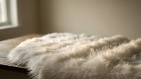 Soft white fur blanket on wooden surface with warm natural sunlight streaming through window creating cozy home interior atmosphere for relaxation and comfort.