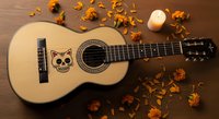 Acoustic guitar with skull design on wooden surface surrounded by autumn leaves and candle for music, day of the dead, or gothic themed projects.