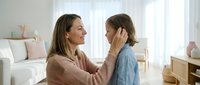 Loving mother gently touching daughter's face in bright modern living room showing family bonding and maternal care between parent and child at home.