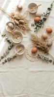 Natural Easter eggs in neutral tones with pampas grass, eucalyptus branches and wooden bowls arranged on white linen for spring holiday decoration.