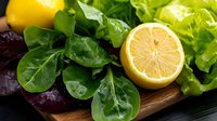 Fresh organic lettuce mix with spinach leaves and cut lemon on wooden cutting board, healthy eating concept for food service and menu design.