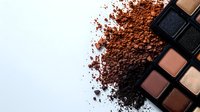 Scattered brown and bronze eyeshadow powder with makeup palette on white background, professional cosmetics flatlay composition for beauty and fashion content.