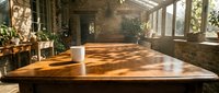 Wooden table in sunlit studio workspace with large windows, potted plants, and brick walls, suitable for product photography, workspace design, and creative business concepts.