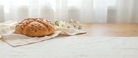 Freshly baked artisan bread loaf with decorative pattern on rustic linen cloth, wooden table surface with soft natural lighting for bakery and food photography.