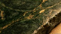 Natural green marble stone surface with golden veins and rough textured edges for luxury interior design and architectural applications.