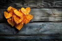 Heart shaped crispy potato chips arranged on rustic dark wooden background with copy space. Orange snacks create romantic mood for party or date.