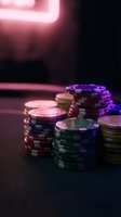 Colorful casino poker chips stacked on dark table with neon lighting creating atmospheric gambling environment for entertainment and gaming concepts.