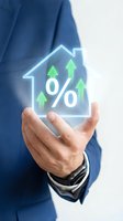 Businessman hand holding glowing house icon with percentage symbol and rising arrows showing mortgage rates growth and real estate investment returns.