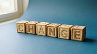 Wooden letter blocks spelling CHANGE on blue surface near window, representing transformation, growth, and new beginnings in business or personal development.
