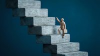 Businessman in formal attire climbing stacked stone blocks against blue background, representing career progression, business growth, and professional achievement in corporate environments.