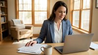 Professional businesswoman working on laptop at home office desk with documents and coffee cup in bright natural light workspace.