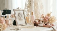 Vintage feminine dressing table with antique photo frame, pearl jewelry, perfume bottles, dried flowers and ballet shoes in soft romantic lighting.